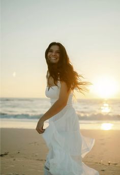 a woman in a white dress is walking on the beach with her hair blowing in the wind