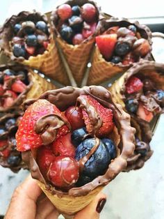 a person holding an ice cream cone filled with chocolate covered strawberries and blueberries