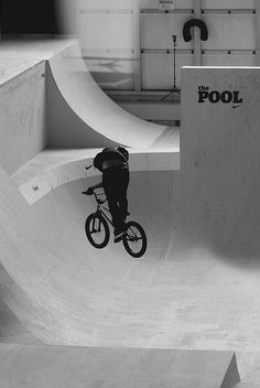 a man riding a bike up the side of a skateboard ramp at a skate park