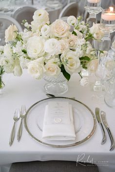 a table set with white flowers and silverware for a formal dinner or wedding reception