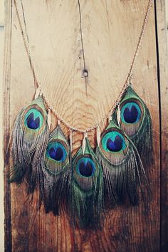 a necklace with peacock feathers hanging from it's side on a wooden board wall