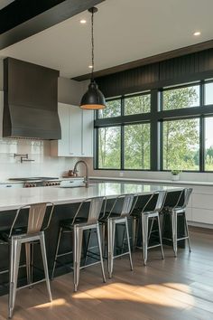 a kitchen with an island and chairs in front of large windows that look out onto the trees outside