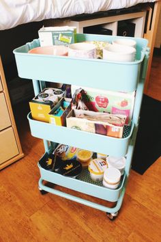 a blue cart filled with lots of items on top of a wooden floor next to a bed