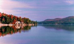 a lake surrounded by mountains and trees in the fall season with red leaves on it