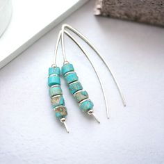 "Handmade Turquoise Threader Earrings. Perfectly suited for everyday boho vibes, these wishbone threaders feature vibrant turquoise jasper for a touch of eye-catching color that won't go unnoticed!  * Sterling Silver * Approximately 1.5\" long * Turquoise Jasper Heishi Beads * Sent in a Ribboned Gift Box with Polishing Cloth * Handmade in Montana  ----- OUR MATERIALS -----  *STERLING SILVER - Experience the elegance of Sterling Silver, a metal that combines versatility with a sophisticated look. Minimalist Turquoise Wire Wrapped Earrings, Adjustable Turquoise Earrings With Ear Wire, Handmade Minimalist Turquoise Hoop Earrings, Silver Threader Earrings, Open Hoop Earrings, Heishi Beads, Threader Earrings, Modern Earrings, Precious Jewelry