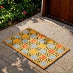 a door mat sitting on the ground next to a wooden door with flowers in it