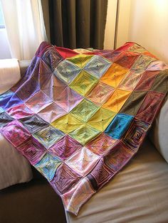 a multicolored blanket sitting on top of a white couch next to a window