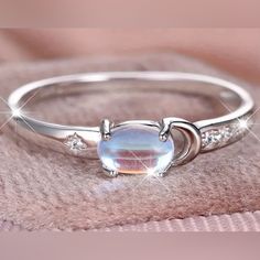 a white gold ring with an opal stone and diamonds on the side, sitting on top of a pink blanket