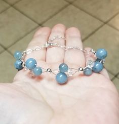 a hand holding a bracelet with blue beads and silver chains on it's wrist