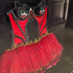 a red and black dress with sequins on the bottom is displayed in front of a fireplace