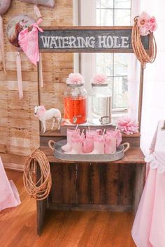 a wooden table topped with lots of pink candles next to a sign that says watering hole