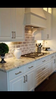 a kitchen with white cabinets and marble counter tops is pictured in this image, there are two vases on the stove