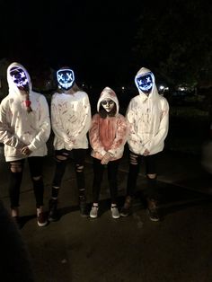 four people in costumes with masks on their faces and hands are standing outside at night