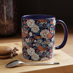 a blue and orange coffee mug sitting on top of a wooden table next to a spoon