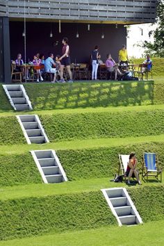 people sitting on lawn chairs in front of a building with grass growing all over it