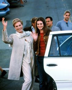 two women waving and standing next to a car