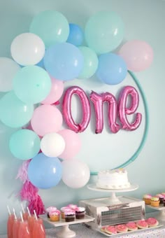 a birthday party with balloons, cake and cupcakes on the table that says one