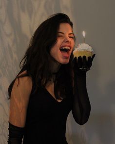 a woman holding a cupcake with a lit candle in her hand and wearing black gloves