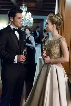 a man in a tuxedo standing next to a woman in a gown holding wine glasses