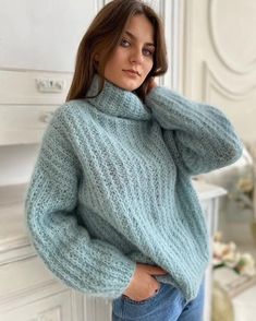 a woman wearing a blue sweater and jeans standing in front of a white dresser with her hands on her hips