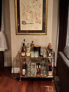 a bar cart filled with liquor bottles and glasses in front of a painting on the wall