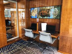 an office with two desks and chairs in front of a large painting on the wall