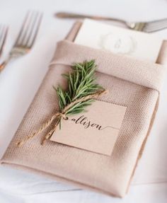 a place setting with napkins, silverware and greenery on top of it