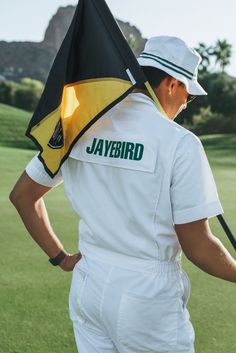 a man holding a black and yellow flag on top of a green golf course with mountains in the background