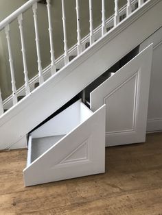 an open drawer underneath a stair case in a room with wooden floors and white railings