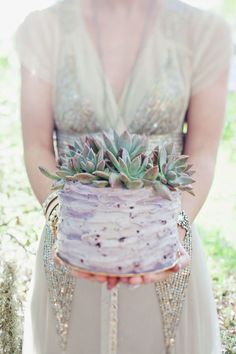 a woman holding a cake with succulents on it