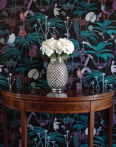 a vase with white flowers on a table in front of a wallpapered background