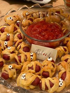 a glass plate topped with pigs in a blanket covered in googly eyes next to a bowl of ketchup