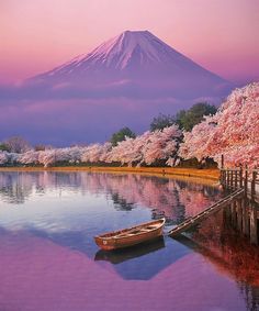 a boat on the water in front of a mountain with cherry blossom trees around it