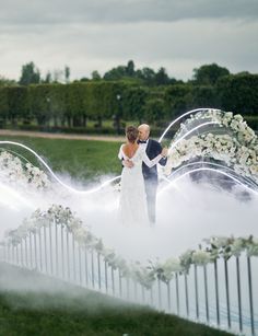 a bride and groom standing in front of a wedding arch with white flowers on it