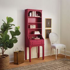 a red bookcase next to a white chair and potted plant