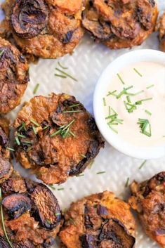 some fried food on a white plate next to a small bowl of ranch dip and sprig of rosemary