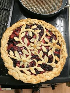 a pie sitting on top of a stove next to a pan filled with fruit toppings