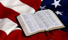 an open book sitting on top of an american flag with the bible in it's lap