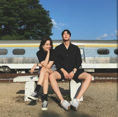 two people sitting on a bench in front of a train