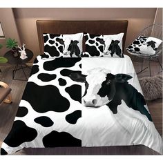 a black and white cow is laying on a bed with two pillow cases in front of it