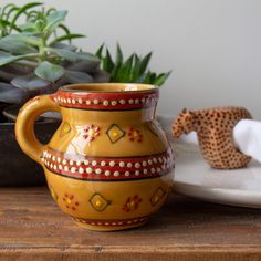 a yellow vase sitting on top of a wooden table next to a potted plant