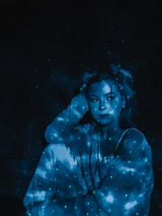 a woman is sitting in the dark with her hands on her head and glowing stars all over her body