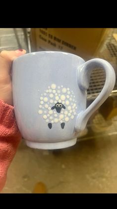 a hand holding a coffee cup with a sheep painted on the side and dots in the middle