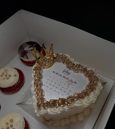 a heart shaped cake in a white box with gold trimmings and decorated cupcakes