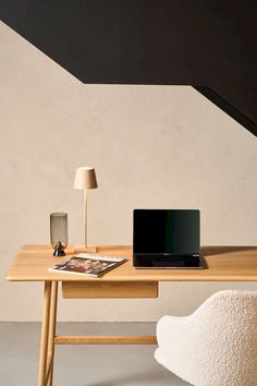 a laptop computer sitting on top of a wooden desk next to a lamp and chair