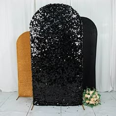 a black and gold sequined chair next to a white wall with flowers on it