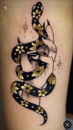 a snake tattoo on the thigh with gold flowers and scissors in it's claws