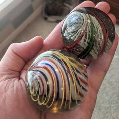 two marbles in the palm of someone's hand, one is multicolored