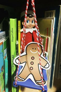 an elf hanging from a book shelf holding a candy cane