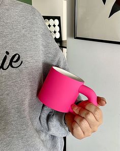 a person holding a pink coffee mug in their left hand and wearing a grey sweatshirt